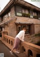 A woman leaning against a stone wall in front of a building.