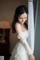 A woman in a wedding dress leaning against a window.