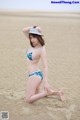 A woman in a bikini and hat on the beach.