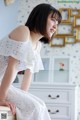 A woman in a white dress sitting on a dresser.