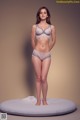 A woman in a gray bra and panties standing on a white pillow.