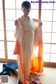 A woman in a white and orange kimono standing in front of a window.