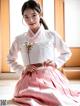 A woman in a pink and white hanbok sitting on the floor.