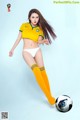 A woman in a yellow shirt and white panties kicking a soccer ball.