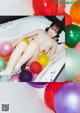 A naked woman sitting in a bathtub surrounded by colorful balloons.