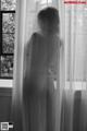 A naked woman standing in front of a window.