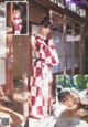 A woman in a red and white kimono leaning against a window.