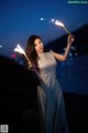 A woman in a long dress holding sparklers in her hands.