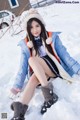 A woman sitting in the snow wearing a blue jacket and boots.