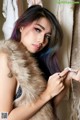 A woman with purple hair wearing a fur vest.