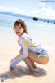 A woman in a bathing suit crouching on the beach.