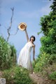 A woman in a white dress holding a straw hat.