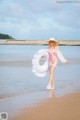 A woman in a pink bathing suit and hat on the beach.