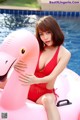 A woman in a red bathing suit sitting on an inflatable flamingo.