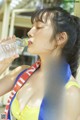 A woman in a yellow bikini drinking water from a bottle.