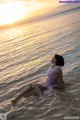 A woman in a pink dress sitting in the water.