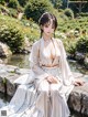 A woman in a white kimono sitting on a rock by a pond.